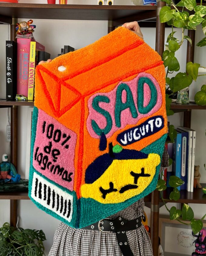 Tapete echo con técnica de tufting en México, de un juguito color naranja y verde con una carita triste que dice Sad Juguito y 100% de lagrimas