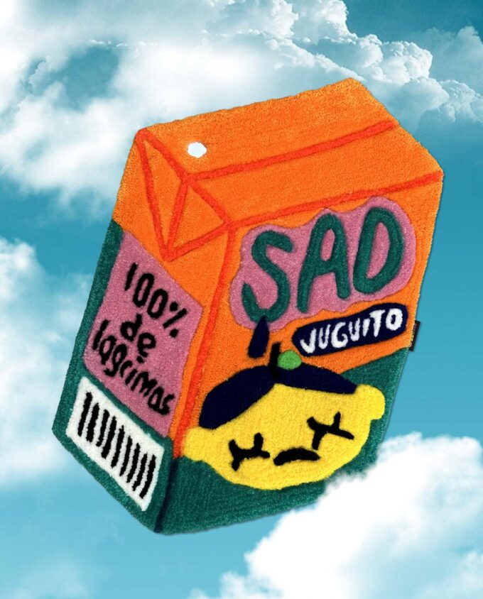 Tapete echo con técnica de tufting en México, de un juguito color naranja y verde con una carita triste que dice Sad Juguito y 100% de lagrimas, en un fondo azul con nubes