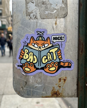 Sticker vinil matte Bad Cat 9x7 cm, gato naranja con gorra leyendo libro de cómo ser un gato malo, contorno recortado ChimChim México
